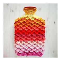 a colorful crocheted vase hanging on a white wooden wall next to a piece of wood