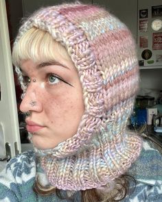 a woman wearing a pink and white knitted hat with a nose piercing in front of a refrigerator