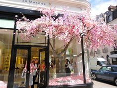 people are walking in front of a store with pink flowers