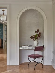 a chair sitting in front of a table with a vase on top of it next to a doorway