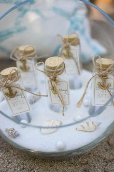 small bottles filled with sand and sea shells on top of a glass bowl, tied with twine