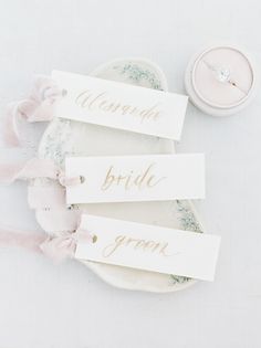 three place cards with names on them sitting on a plate next to a wedding ring