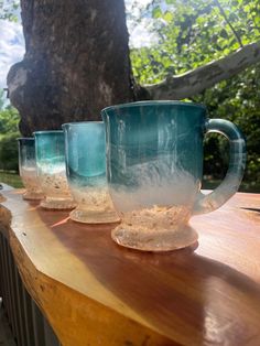 four glass mugs sitting on top of a wooden table in front of a tree