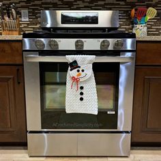 a knitted snowman scarf hanging on an oven door in a kitchen with wooden cabinets and stainless steel appliances