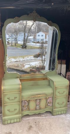 a green dresser with a mirror on the top and drawers below it in front of a house