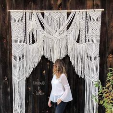 a woman standing in front of a white macrame wall hanging on a wooden fence