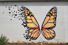 a large butterfly painted on the side of a white brick building with lots of black birds flying around it