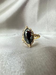 a gold ring with a black stone in the center on a white cloth background,