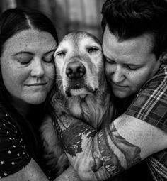 a man and woman hugging their dog in front of the camera, black and white photo