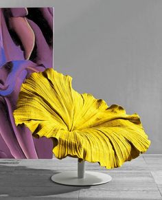 a yellow flower sitting on top of a white pedestal in front of a large painting