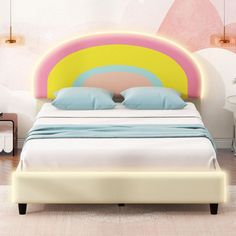 a white bed with blue and yellow pillows in a room that has pink, yellow, and green accents on the walls