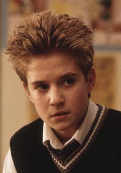 a young man with blonde hair wearing a sweater vest