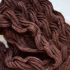 a knitted scarf laying on top of a white blanket covered in brown yarns