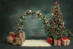 a christmas tree with presents under it and a teddy bear sitting next to it on a rug