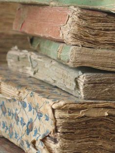 stack of old books sitting next to each other on top of a wooden tablecloth