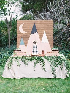 a table topped with cake and desserts on top of a grass covered field next to trees