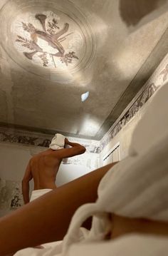 a man in white shirt laying on top of a bed next to a ceiling mural