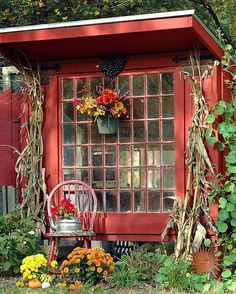 a red shed with flowers and plants around it