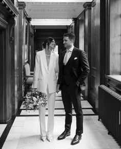 a man and woman in formal wear walking down a hall way with flowers on the floor