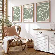 a white chair sitting next to a wooden dresser under three framed art prints on the wall