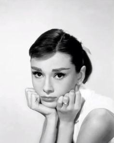 a black and white photo of a woman with her hands on her chin, looking at the camera