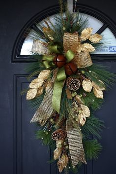 a wreath with pine cones and evergreen leaves hanging from the front door on a black door