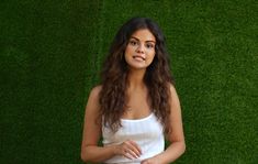 a woman standing in front of a green wall with her hand on her hip and looking at the camera