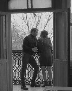 black and white photograph of two people standing in front of an open door looking at each other