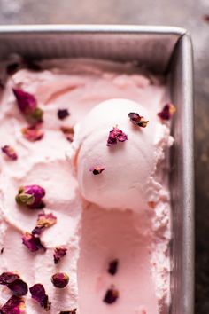 a scoop of ice cream in a metal container with pink flowers on top and petals scattered around it