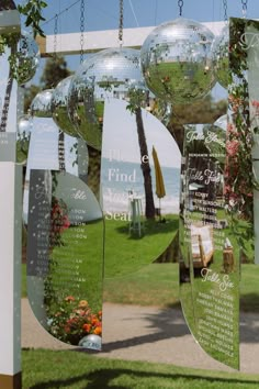 several mirrored balls hanging from the ceiling in front of a tree and grass area with flowers