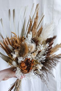 a person holding a bouquet with dried flowers and feathers in it's palm, on a white background