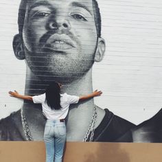 a woman standing in front of a wall with a mural of a man's face on it