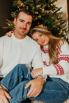 a man and woman sitting next to a christmas tree