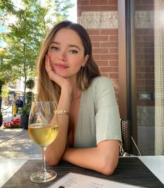 a woman sitting at a table with a glass of white wine in front of her