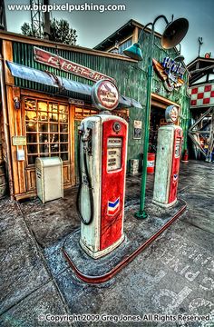 an old gas station with two red and white pumps in front of the storefront