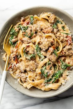 a bowl filled with pasta, meat and spinach on top of a marble table