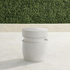 a white container sitting on top of a cement floor next to a green hedge wall