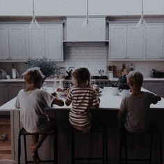 three children are sitting at the kitchen counter looking out over the sink and eating food