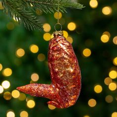 a red ornament hanging from a christmas tree with lights in the back ground