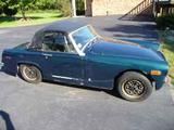 an old blue sports car parked on the side of the road in front of a house