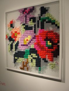 a cross stitch picture hanging on the wall next to a white frame with flowers in it