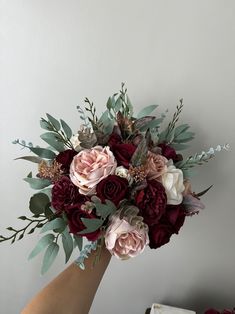 a hand holding a bouquet of red and pink flowers with greenery on the stems