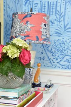 a vase with flowers sitting on top of a table next to books and a lamp