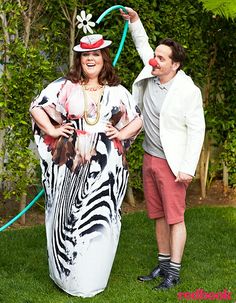 two people standing in the grass with one holding a hose and another wearing a costume