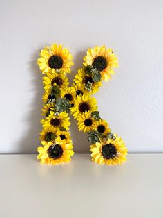 the letter k is made up of sunflowers and greenery in front of a white wall