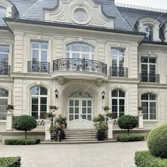 a large white building with many windows and balconies on the top floor, surrounded by hedges