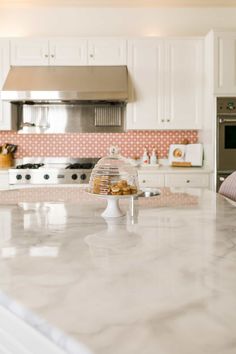 a large kitchen with white cabinets and marble counter tops in front of the stove top