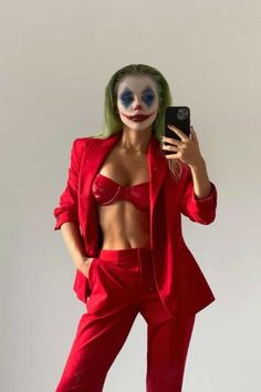 a woman dressed as the joker taking a selfie with her cell phone while wearing a red suit