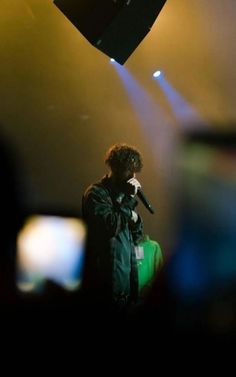 a man standing on top of a stage holding a microphone in his hand and wearing a green shirt