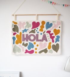 a wall hanging with the word hola painted on it and hearts in different colors